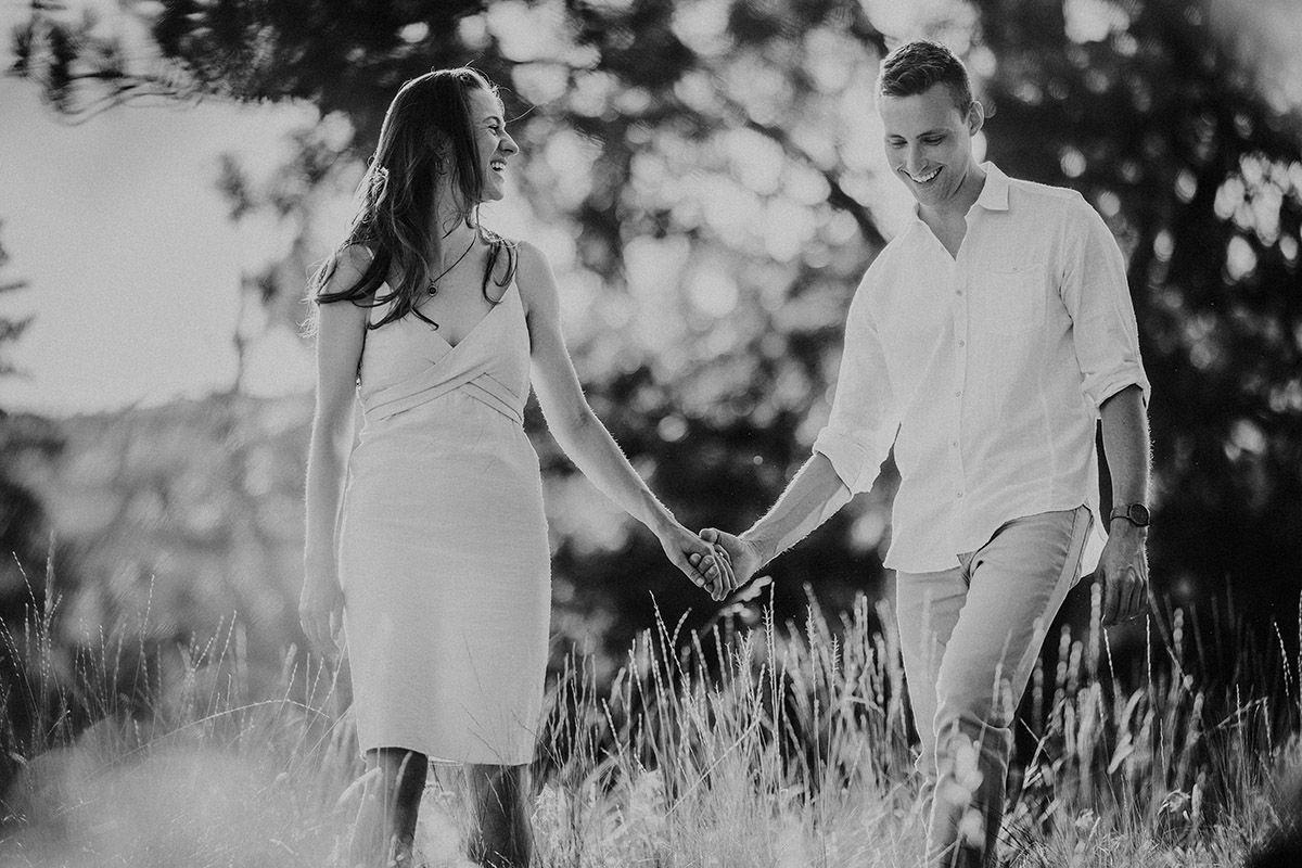 Black and white photo of a couple holding hands and walking through a grassy field surrounded by trees.