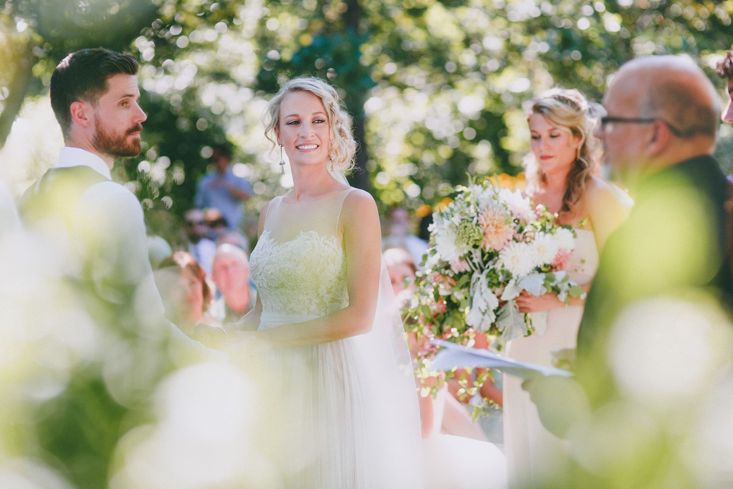 A romantic outdoor wedding ceremony in a sunlit garden setting with floral decorations and guests in attendance.
