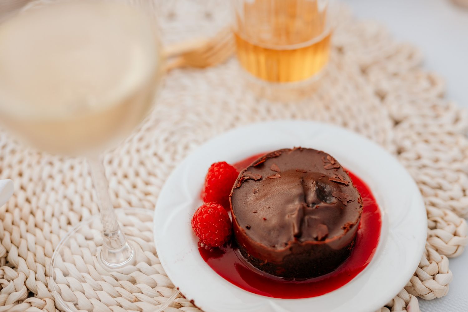 A chocolate dessert with raspberry sauce sits on a white plate against a lace doily background.