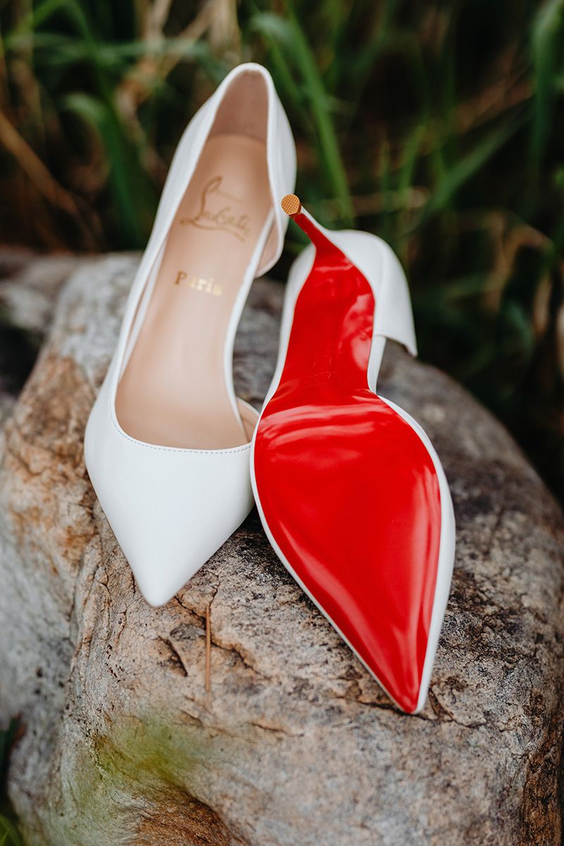 A pair of red and white high heel shoes displayed on a rustic log in an artistic fashion photography setup.