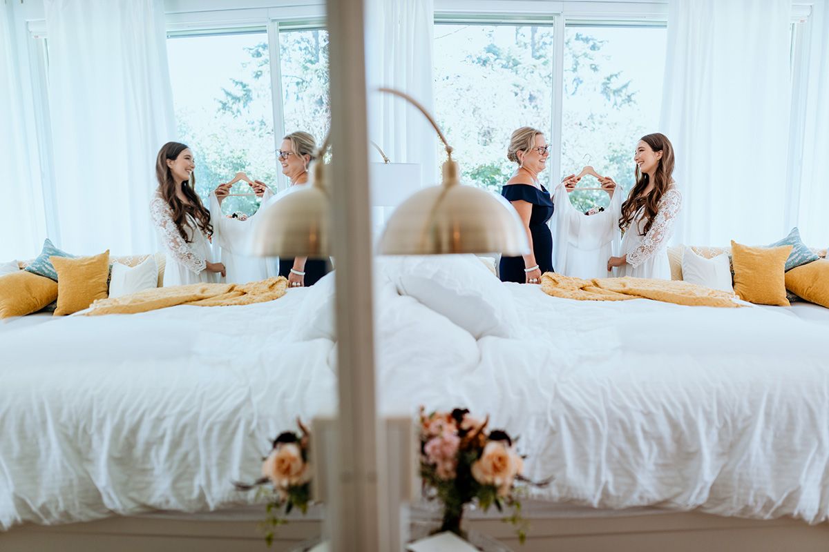 A bride and her mother in a bright, modern bedroom with yellow pillows.