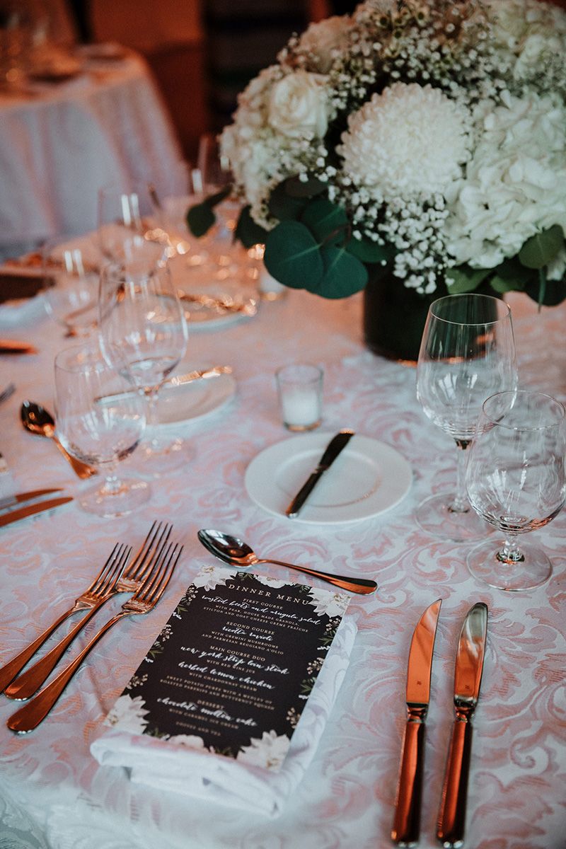 Elegant wedding reception table settings with white floral centerpieces, pink damask tablecloths, and black menu cards.