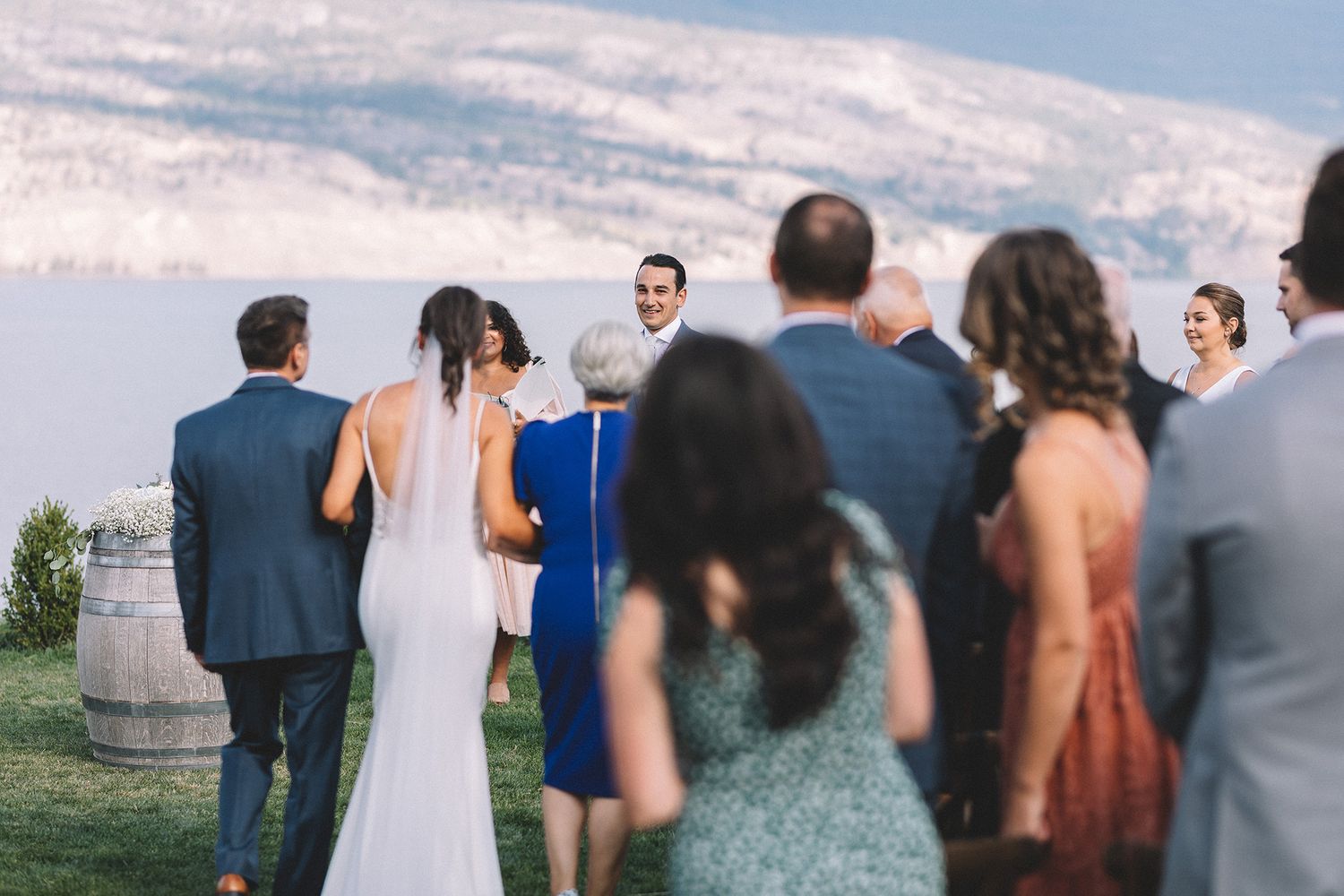 Wedding guests stand in a row outdoors during a ceremony against a scenic mountain backdrop.