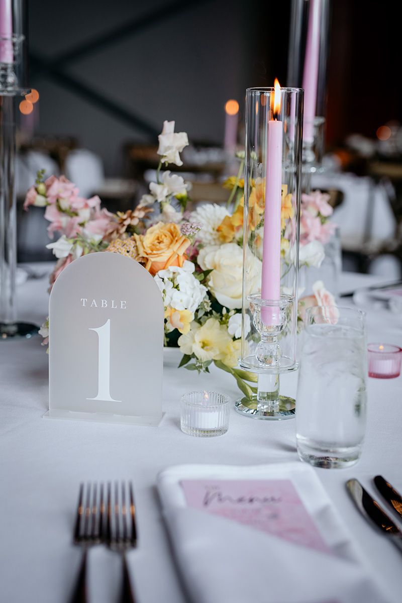 Elegant wedding reception table setting with pink candles, floral centerpieces, and table number one displayed.