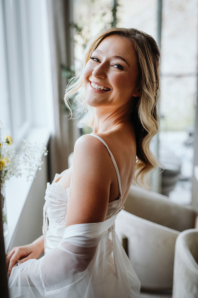 Intimate boudoir photography series showing a bride to be in white lingerie posing on a couch near windows in natural light.