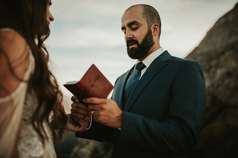 A groom reads from his leather-bound vow book during a mountain-top golden hour wedding ceremony.