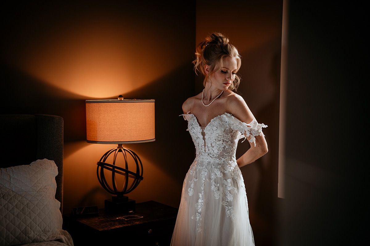 A romantic wedding dress detail shot illuminated by warm ambient lighting in a dark room.