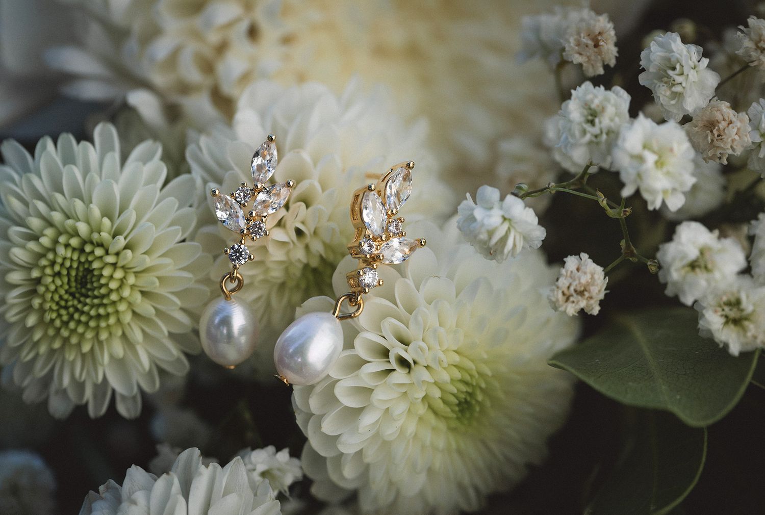 Pearl earrings nestled among an elegant floral arrangement white chrysanthemum and small delicate flowers.