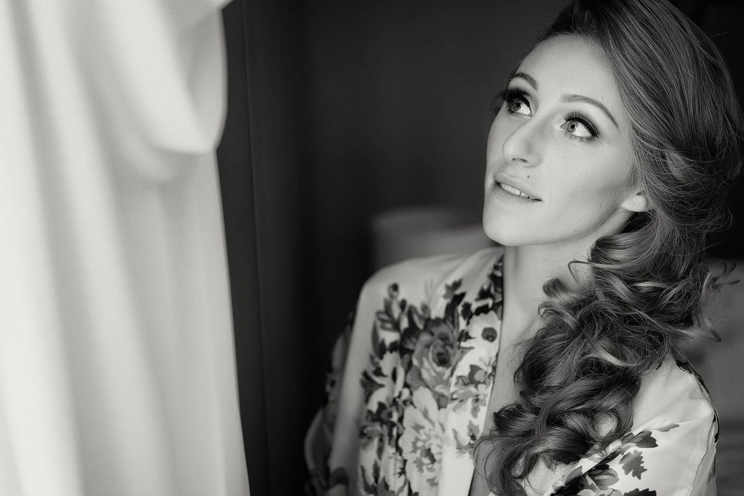Glamorous black and white portrait of a woman with curled hair and dramatic makeup looking to the side.