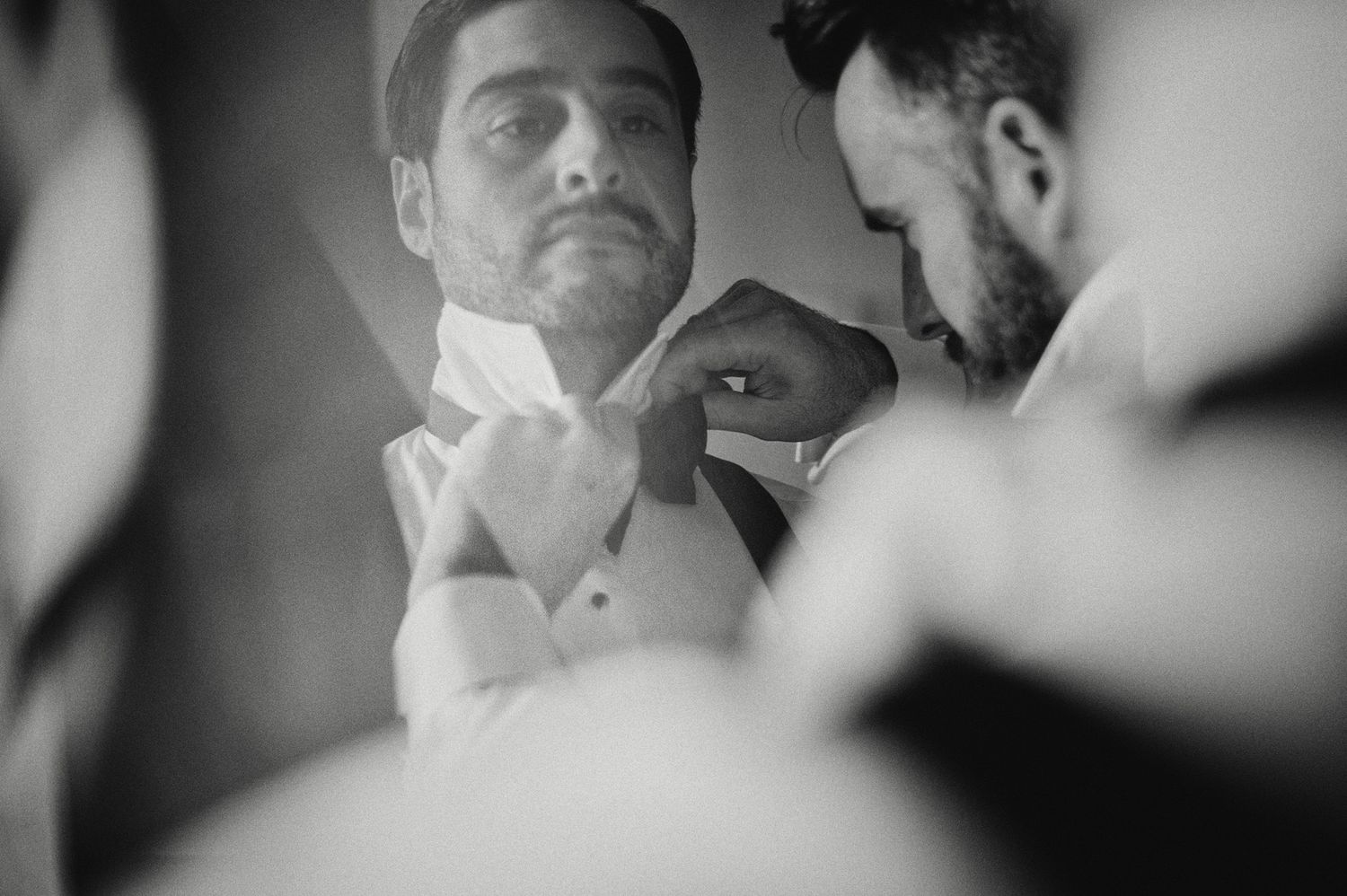 Black and white image of a best-man helping a groom with his bow-tie.
