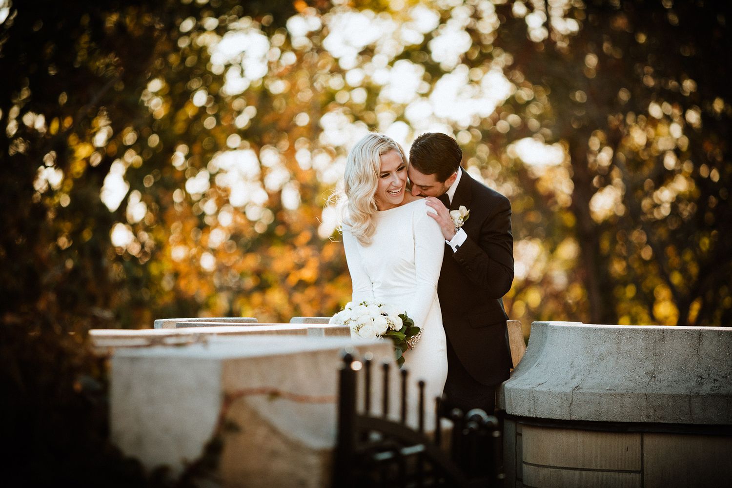 A couple shares an intimate moment during their wedding photoshoot in a golden sunset-lit garden setting.