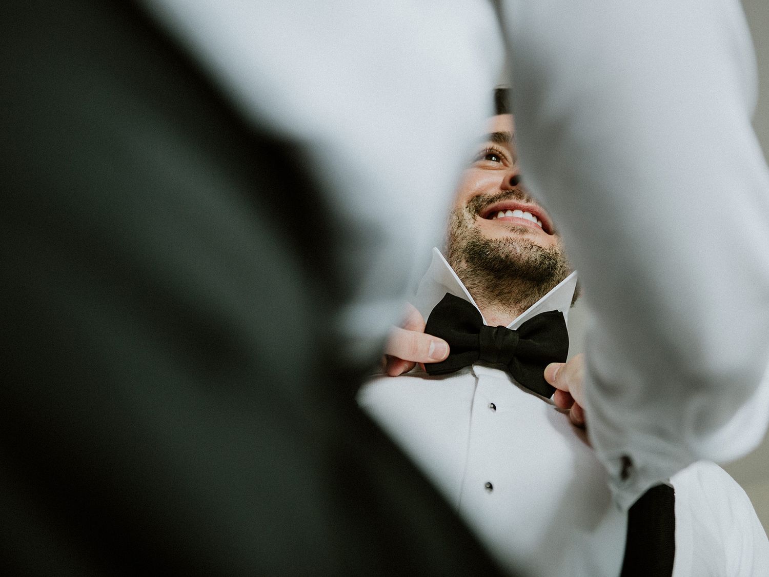 Close-up profile view of groom wearing a black bowtie and white dress shirt looking upward.