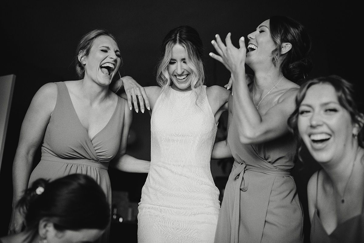 Black and white candid photo showing joyful wedding party members laughing together during celebration.