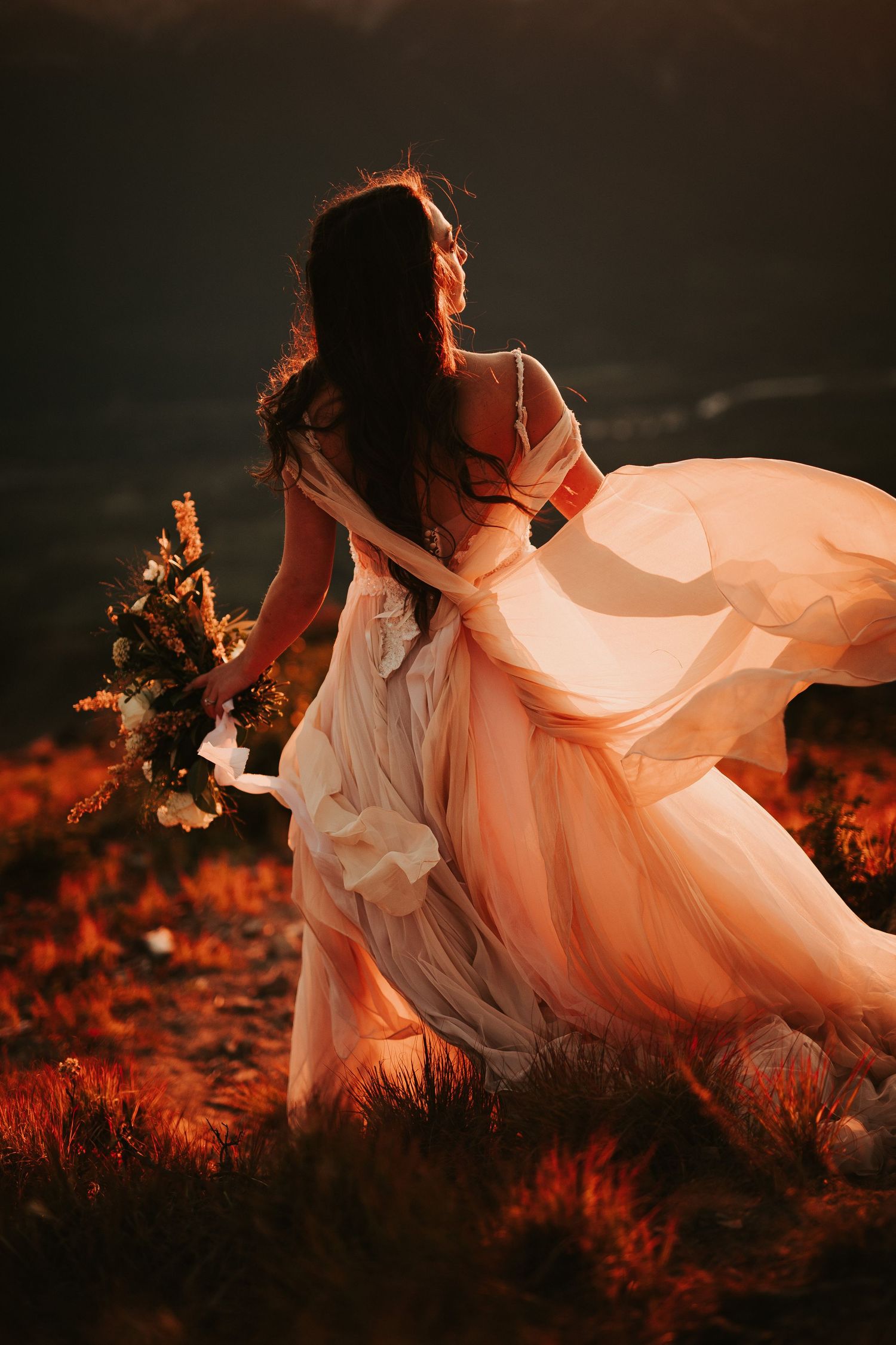 A flowing white dress catches the golden sunset light as a bride moves gracefully through red autumn grass.