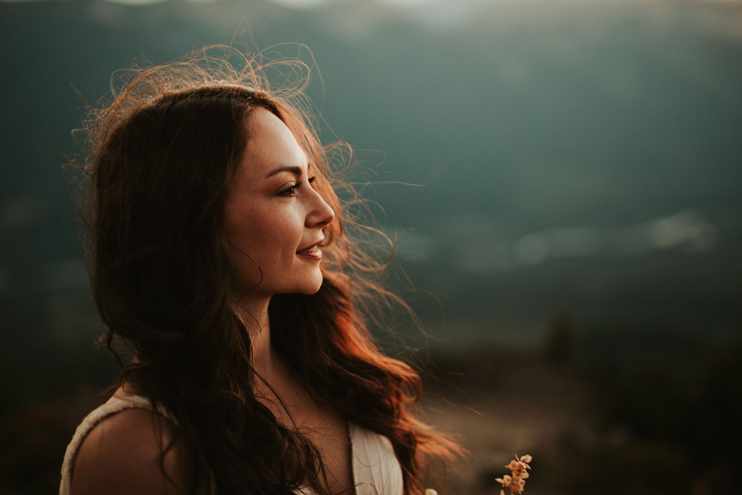A bride with flowing hair stands against a dramatic sunset sky in a series of moody outdoor portraits.