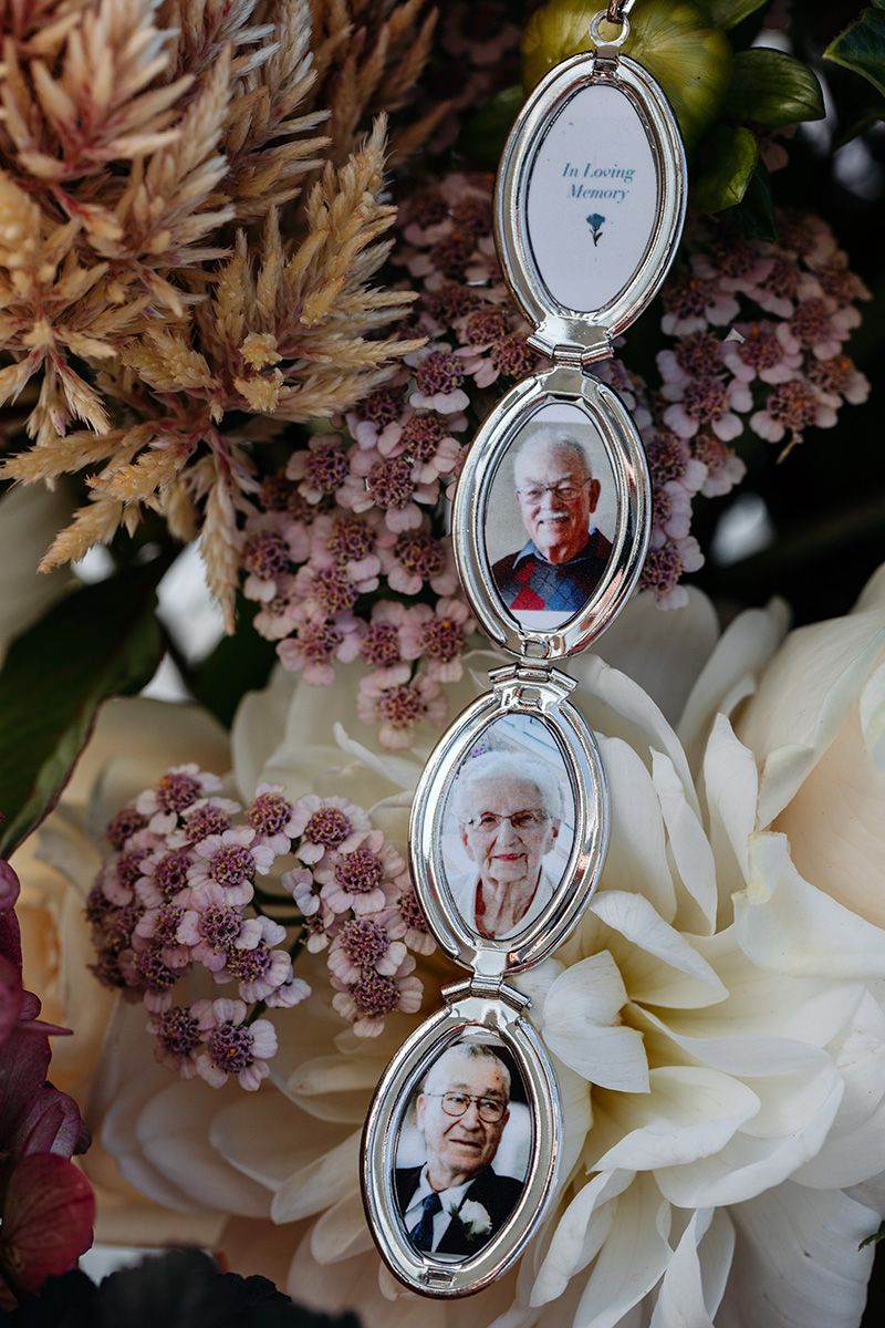 A silver locket charm containing photos of deceased relatives hangs in front of white flowers and pink blossoms.