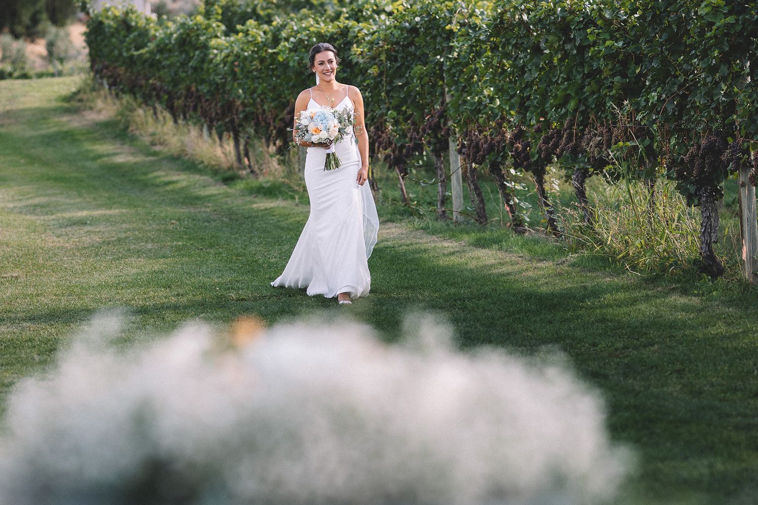 A bride in a flowing white wedding dress walks through a lush garden setting during an outdoor photo session.