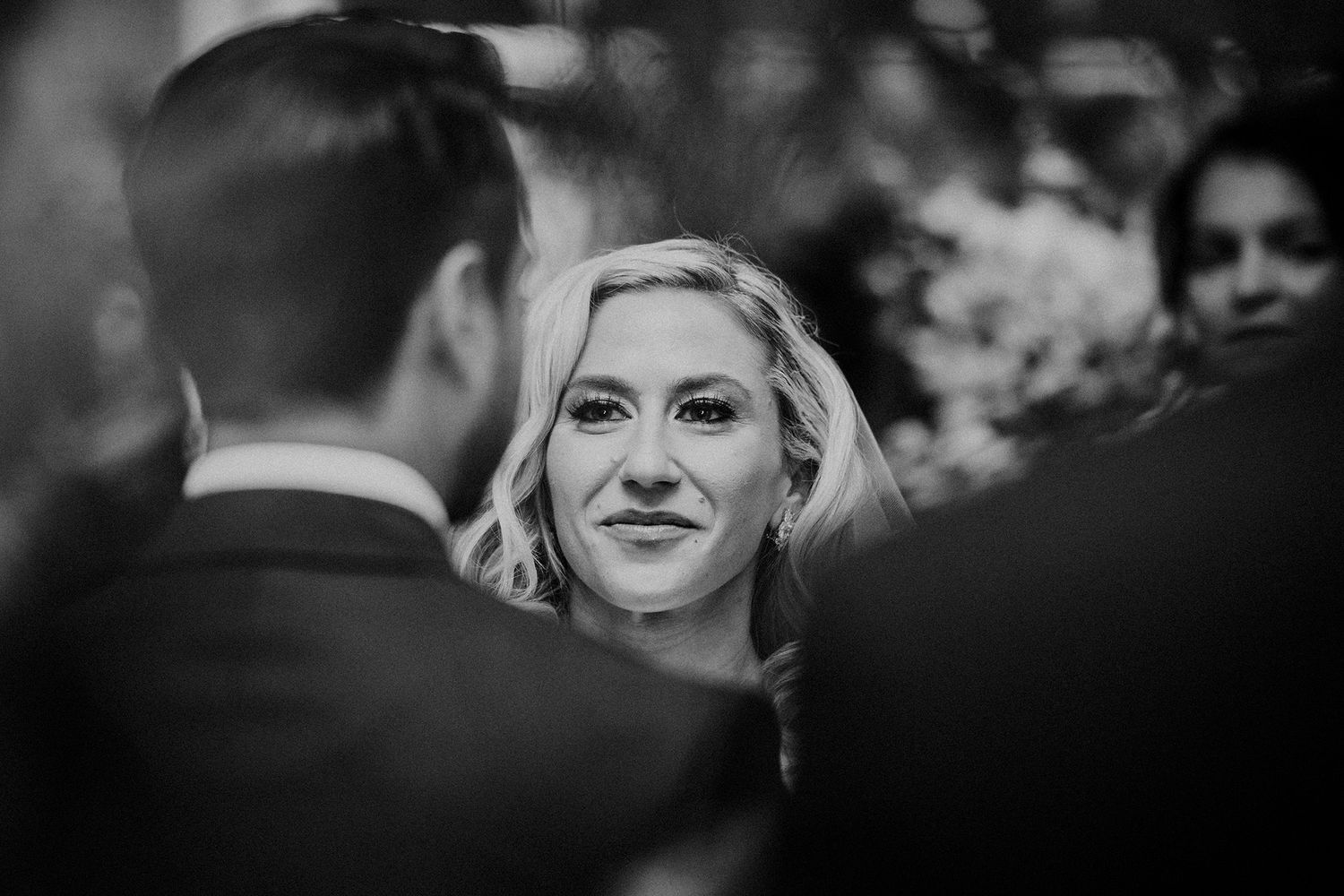 A black and white photo showing a bride looking lovingly at her groom during their indoor wedding ceremony.