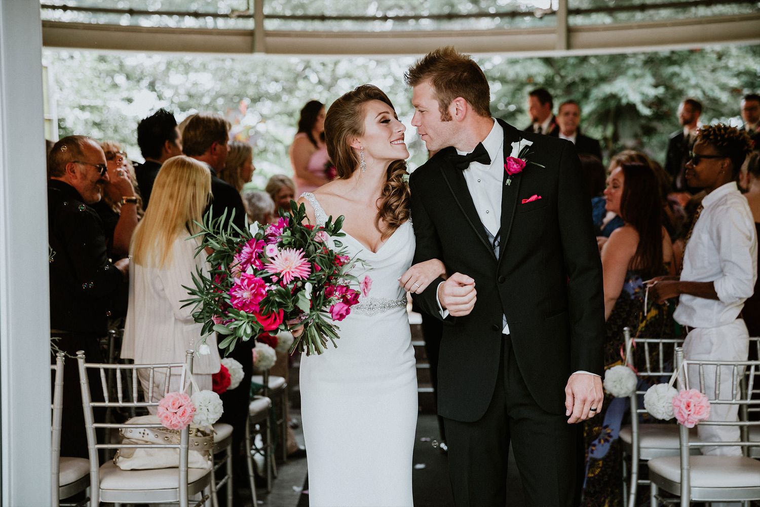 Wedding couple shares intimate moments during outdoor reception under white tent with floral decorations and guests.