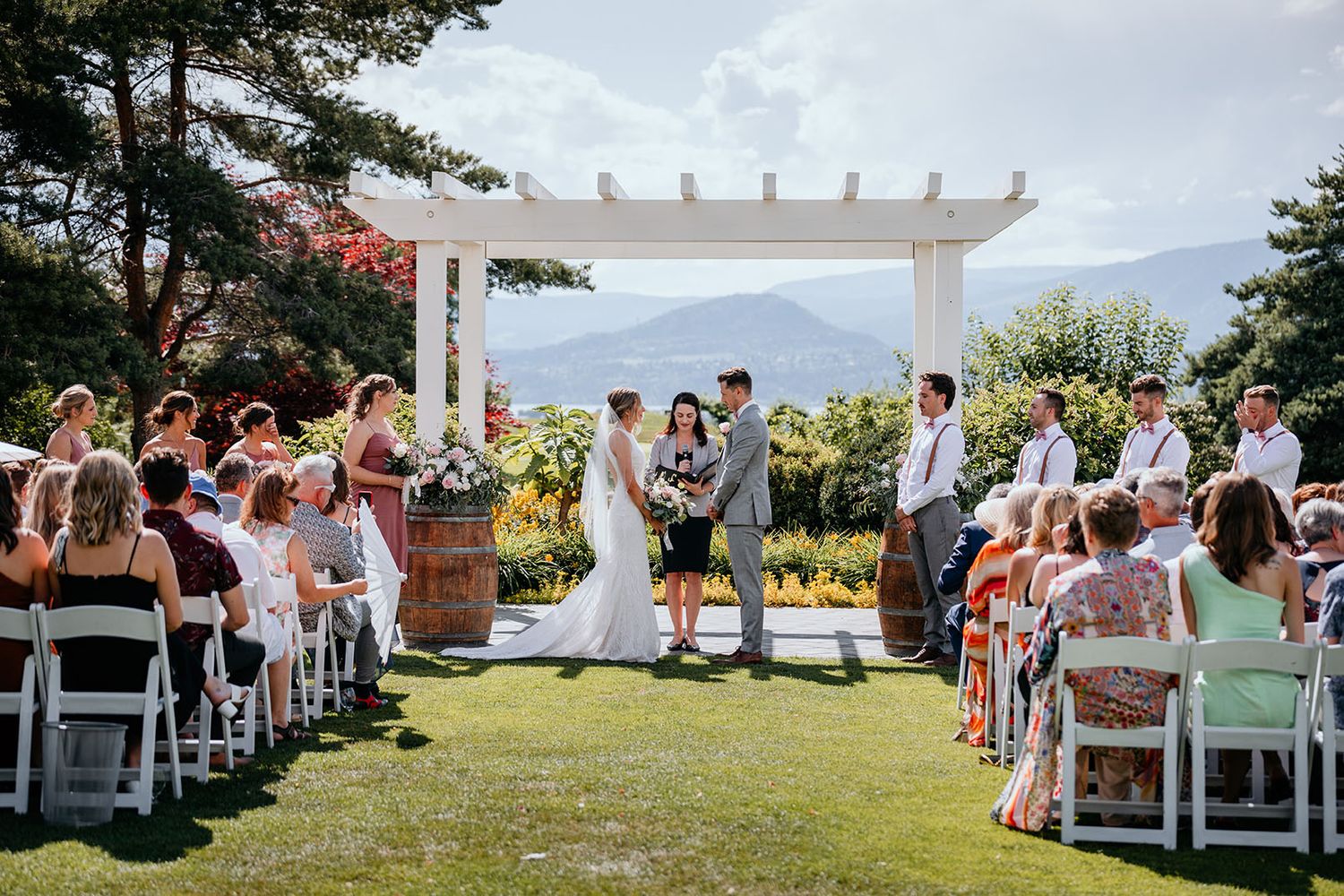 Outdoor wedding ceremony setup with white chairs and pergola overlooking a scenic mountain landscape.
