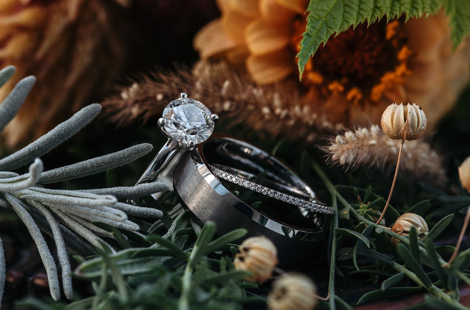 Close-up macro shot of a diamond engagement ring with a floral background and natural lighting.
