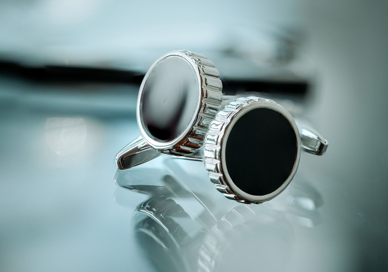 Chrome plated cufflinks with dark inlaid centers arranged in a row against a teal-toned background.