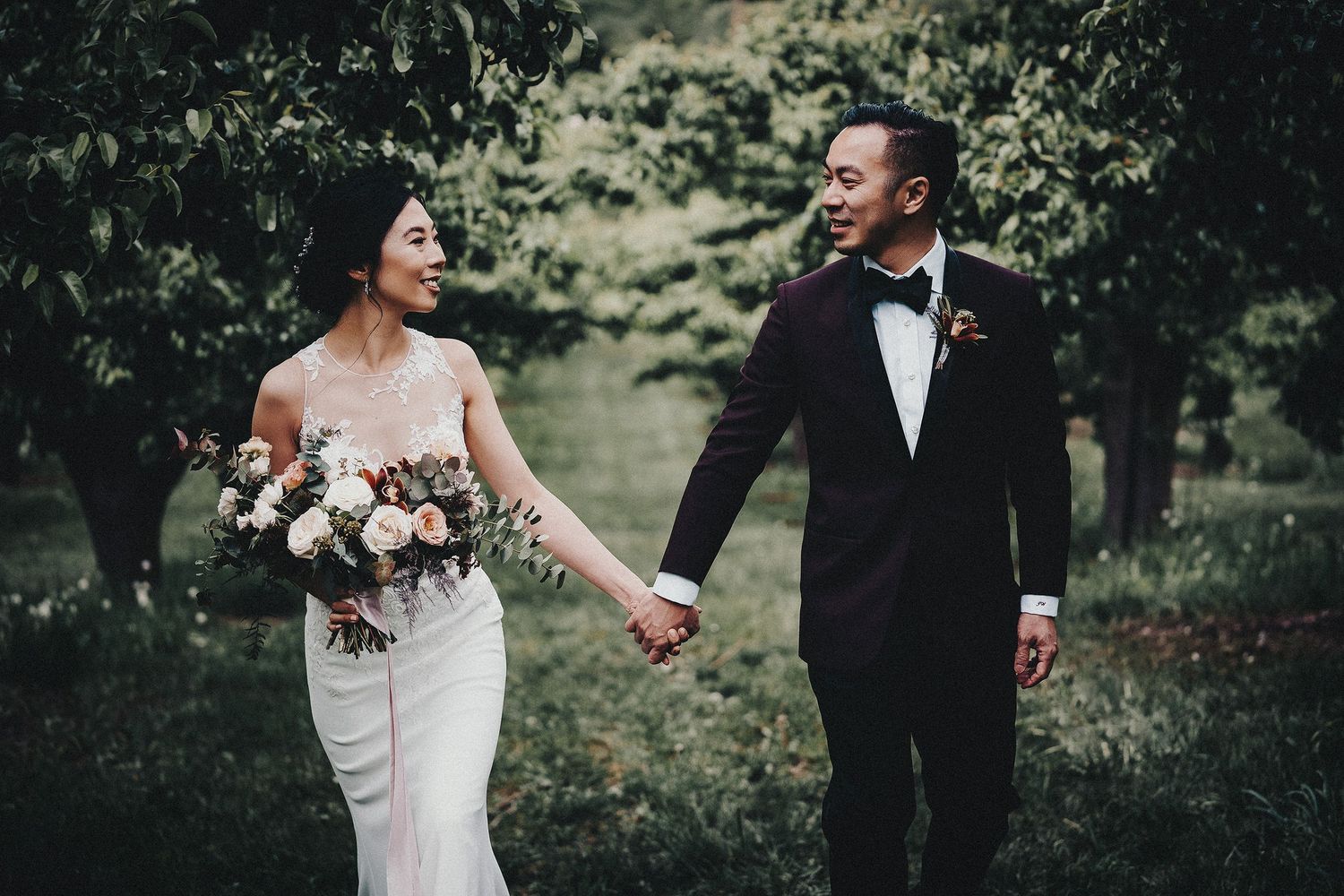 An Asian wedding couple walking through an orchard before heading to their Summerhill Pyramid Winery wedding.