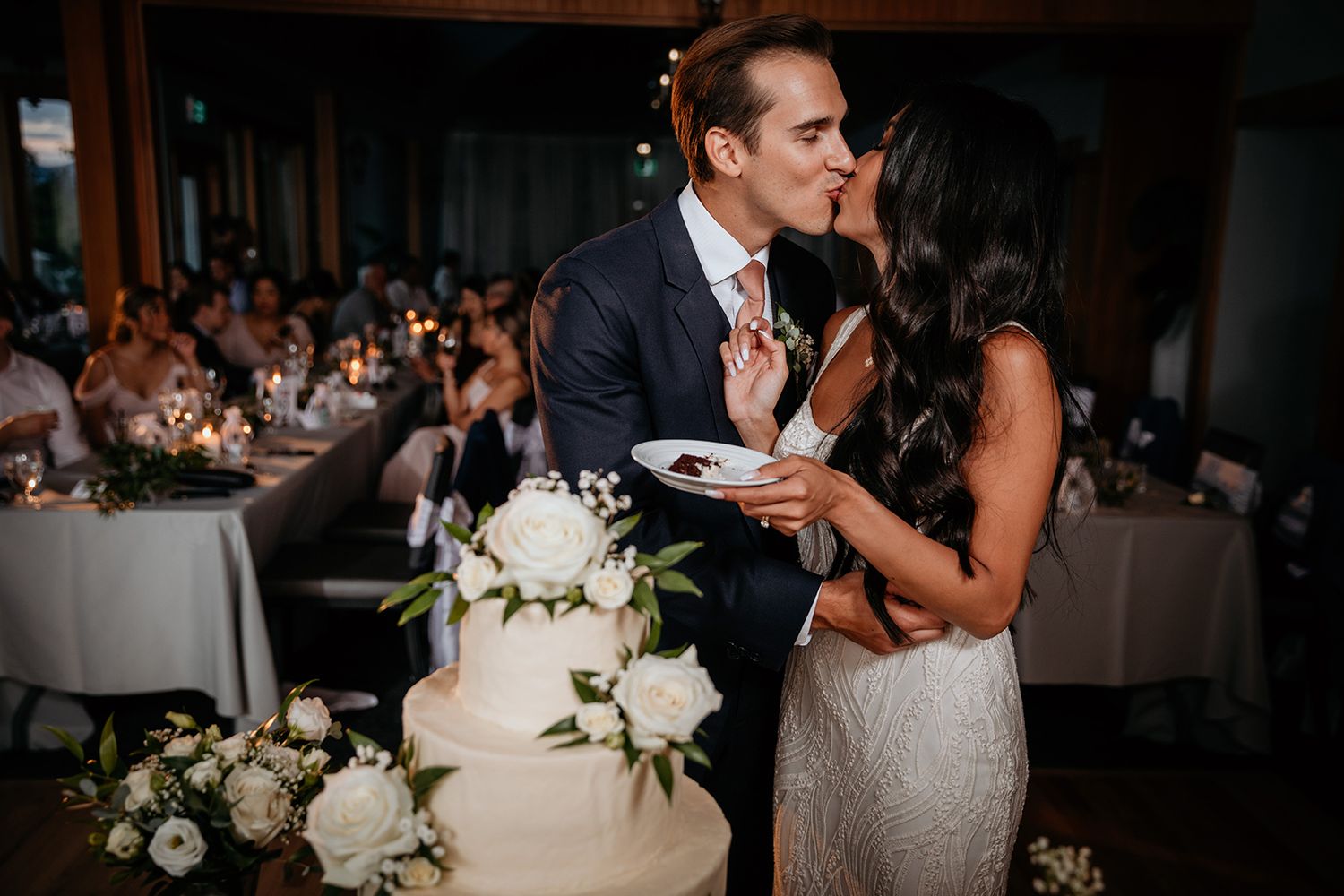 A groom and his bride enjoy a kiss while feeding each other a bite of their wedding cake. The Harvest Golf Club in Kelowna, BC