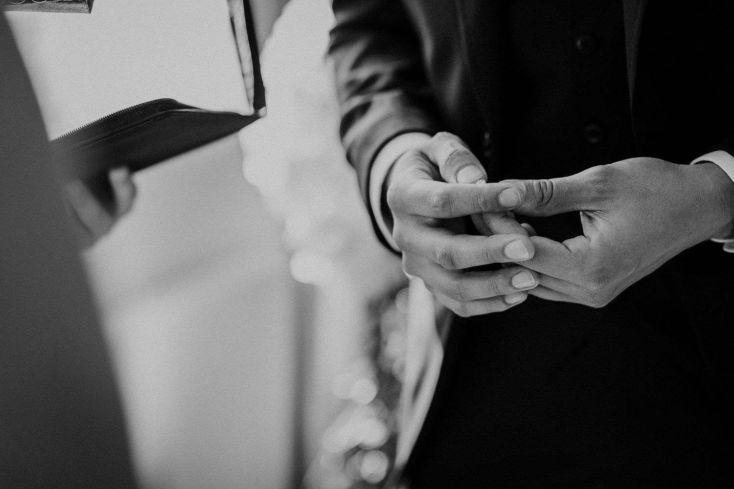Black and white photo of a groom's hands holding his bride's wedding ring.