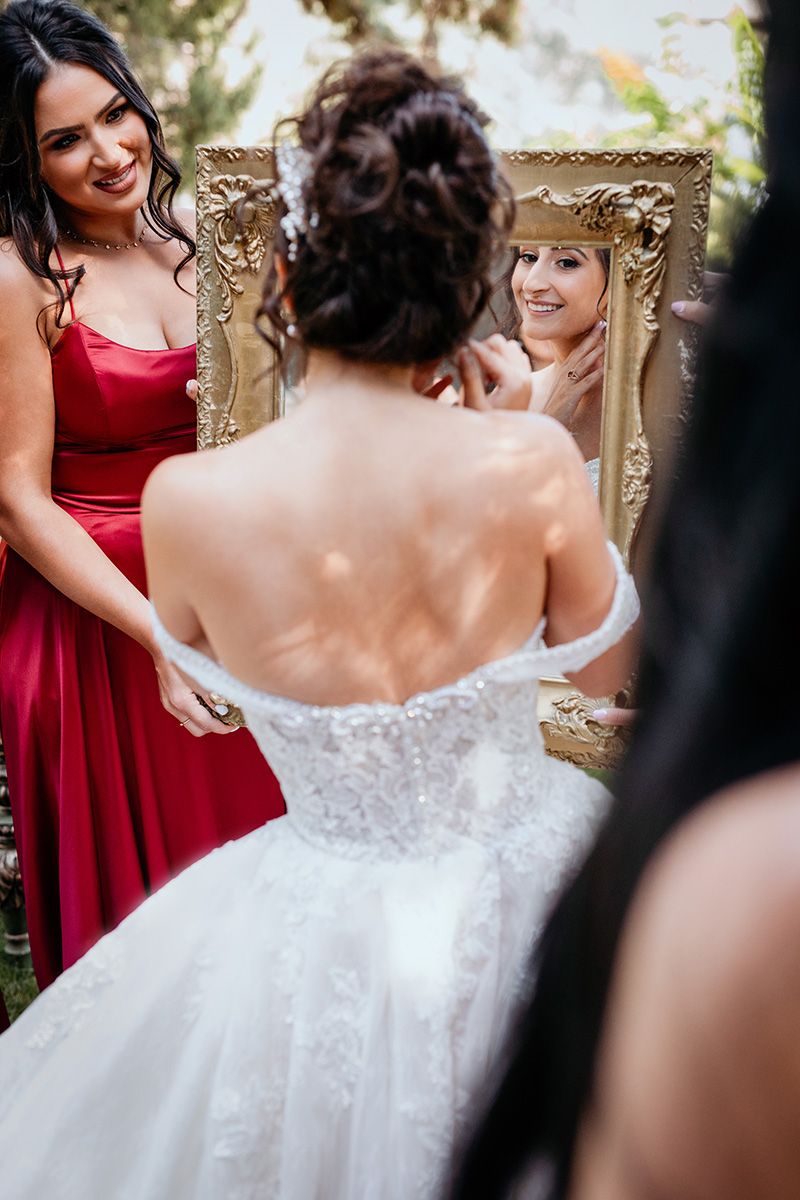 Wedding party members in red bridesmaid dresses help a bride with her earrings.