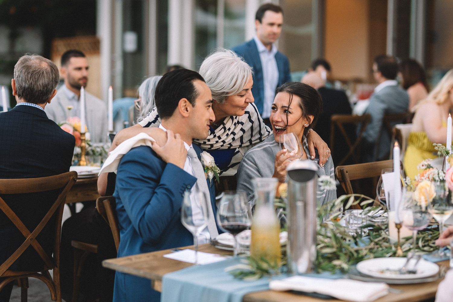 Wedding guests enjoy an elegant outdoor dining experience at long tables decorated with floral centerpieces.
