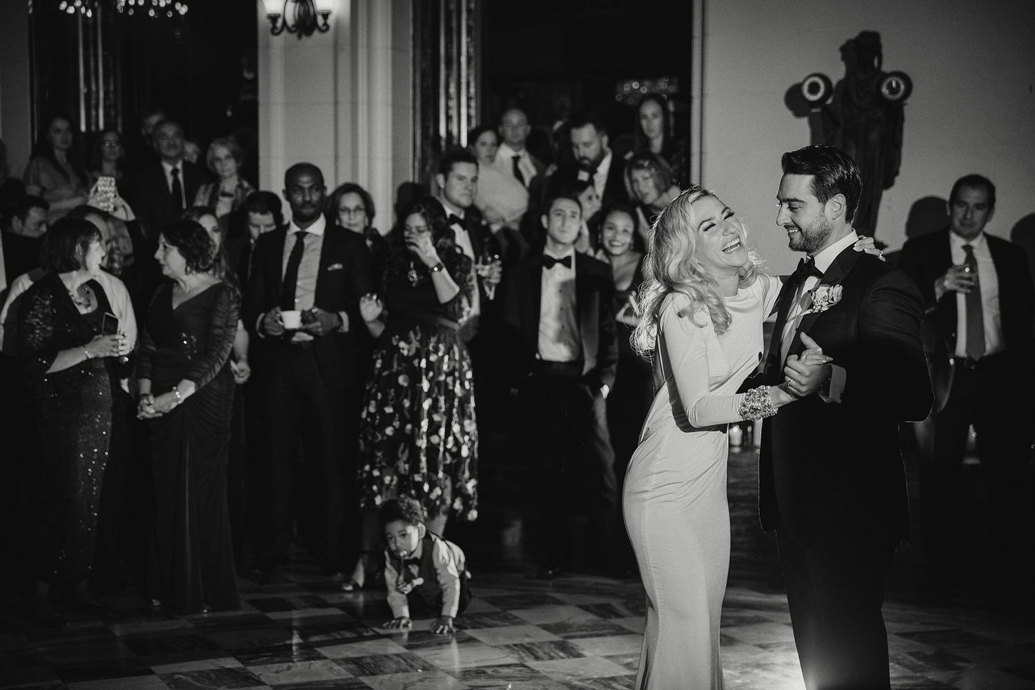 A black and white photo of people dancing and celebrating at an elegant formal event in evening attire.