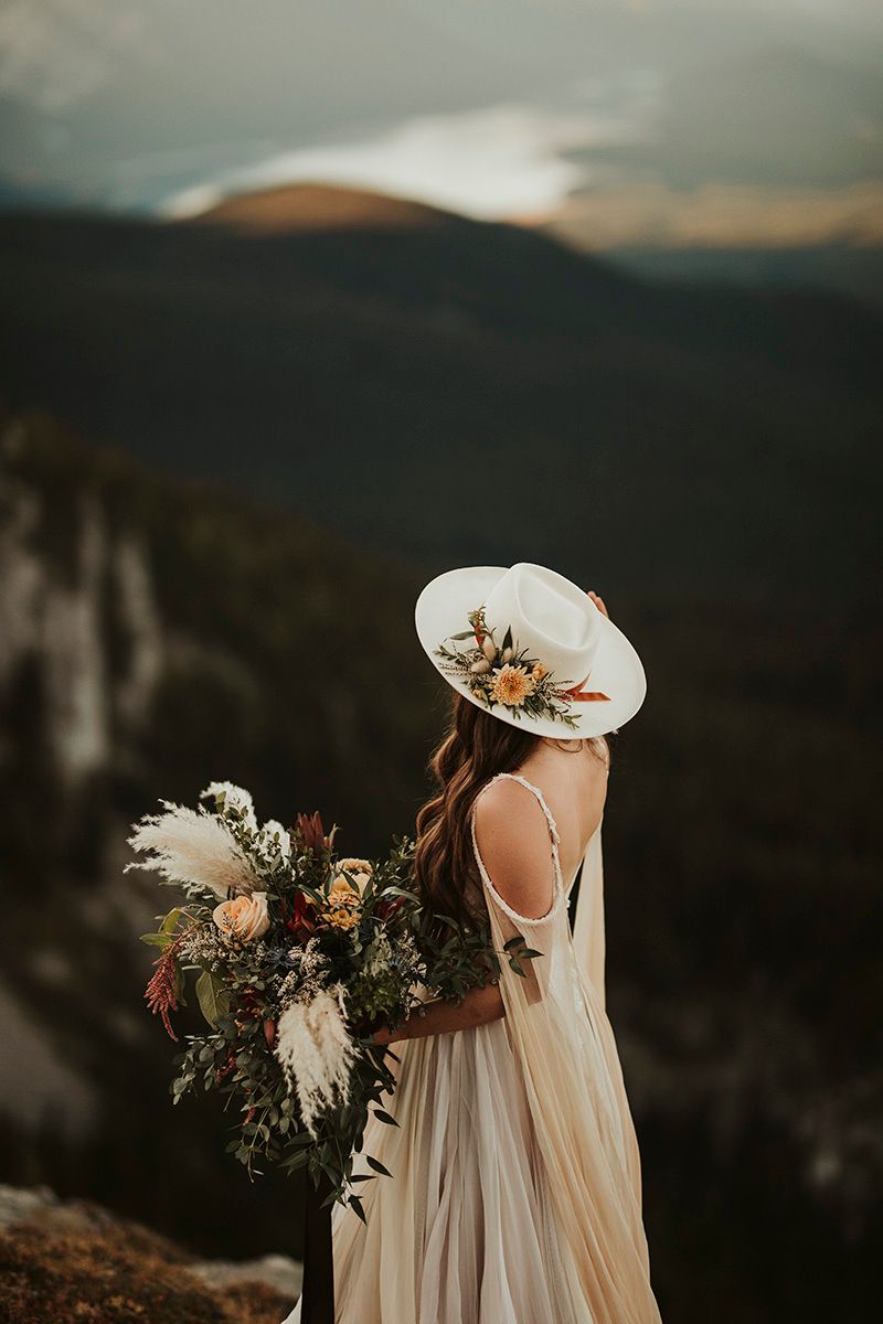 Ethereal wedding dress flows in the wind against a dramatic mountain landscape at sunset.