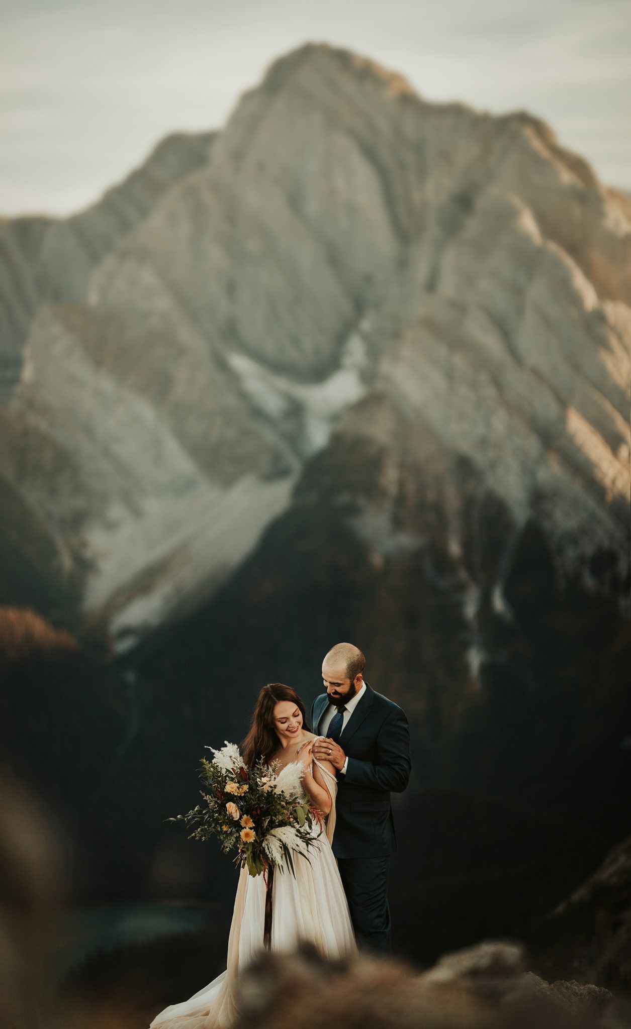 A romantic wedding couple embraces against a backdrop of majestic mountain peaks during golden hour.