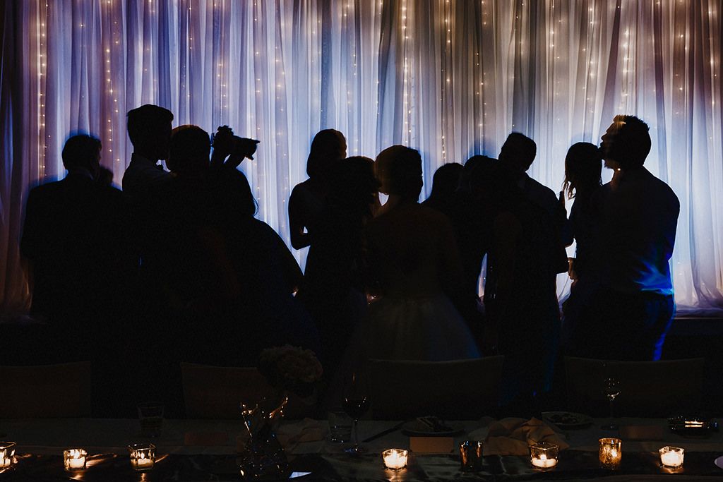 Silhouettes of people standing in front of illuminated white curtains at an indoor event.