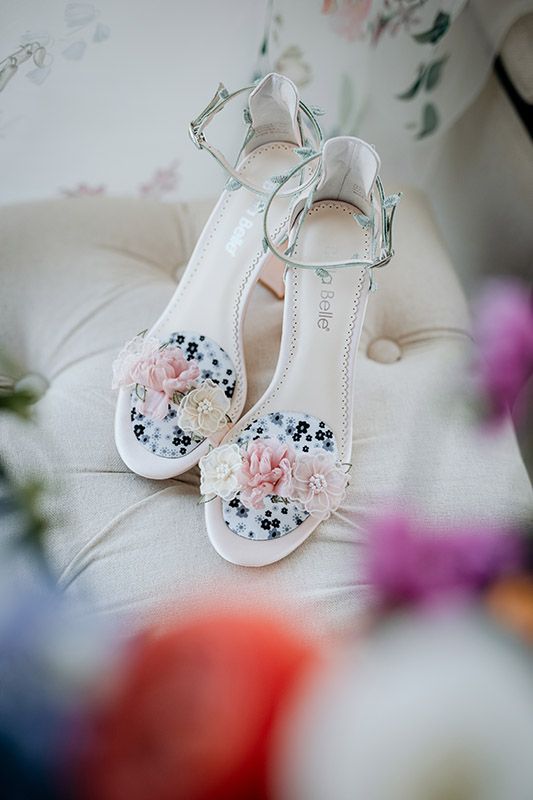 Delicate white bridal shoes with pink floral accents and navy blue details shown in a soft focus composition.