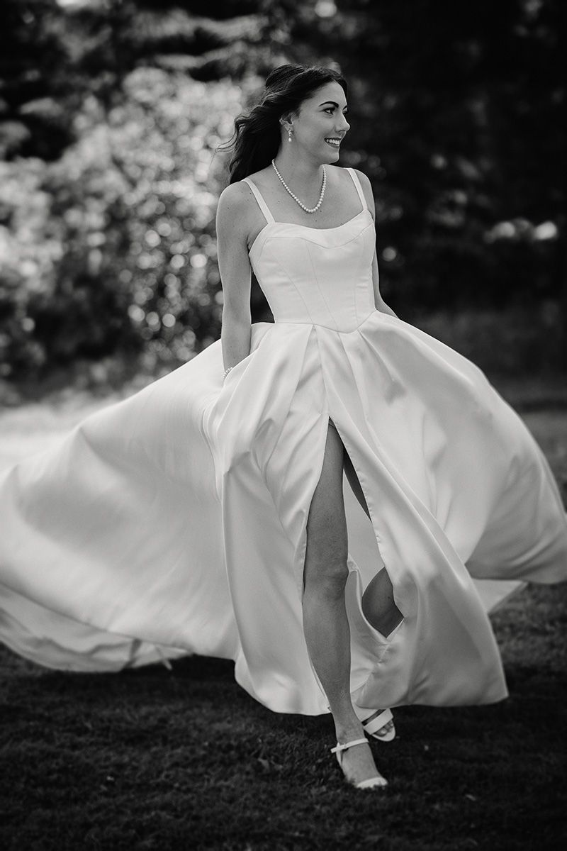 A bride in a flowing white wedding dress twirls gracefully in a black and white artistic photo.