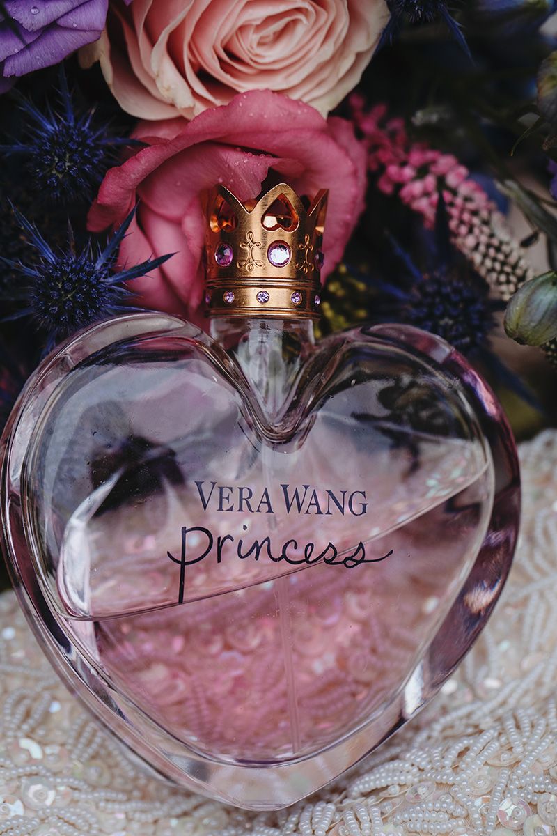 Vera Wang Princess perfume bottle with pink liquid and crown-shaped cap displayed on lace fabric.