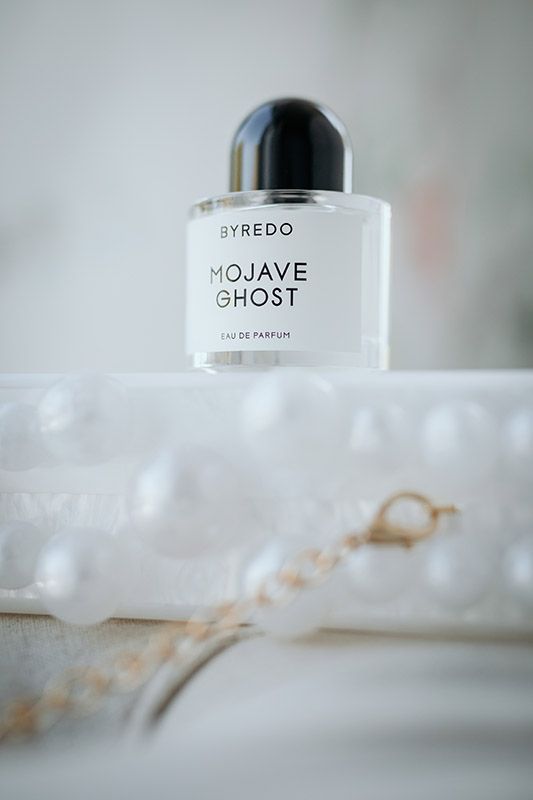 Luxury perfume bottles from Byredo, Mojave, and Ghost brands arranged on a white surface with soft, dreamy lighting.