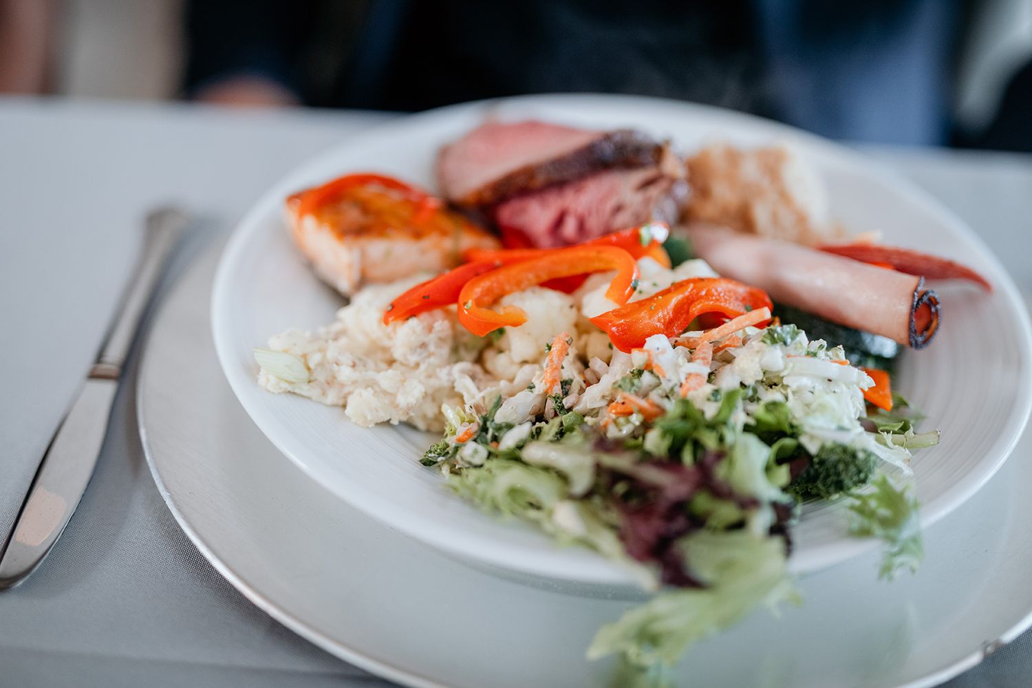 A plate of rice pilaf served with sliced ham, mixed vegetables, and fresh salad on a white dish.