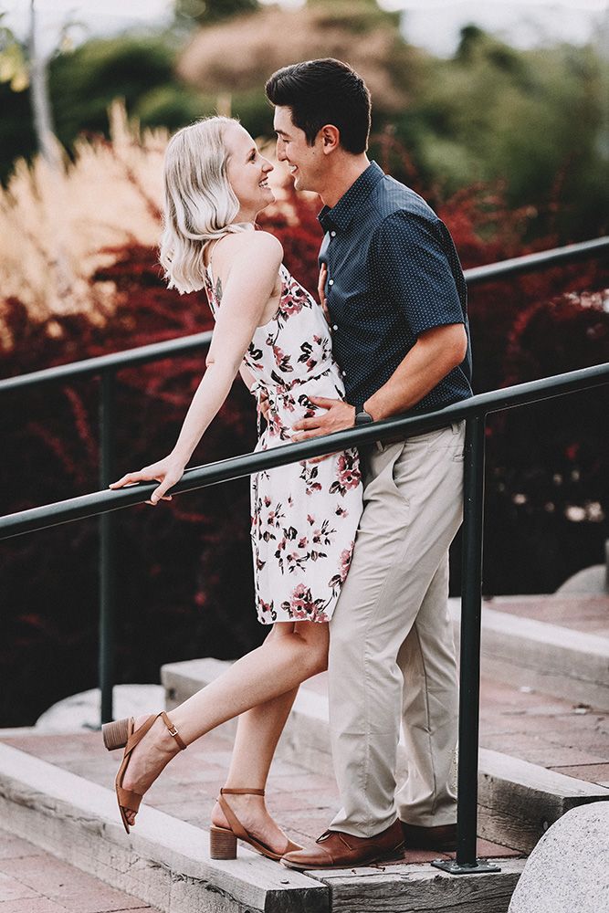 Romantic couple embraces and shares intimate moments along a railing in a garden setting during an engagement photo session.