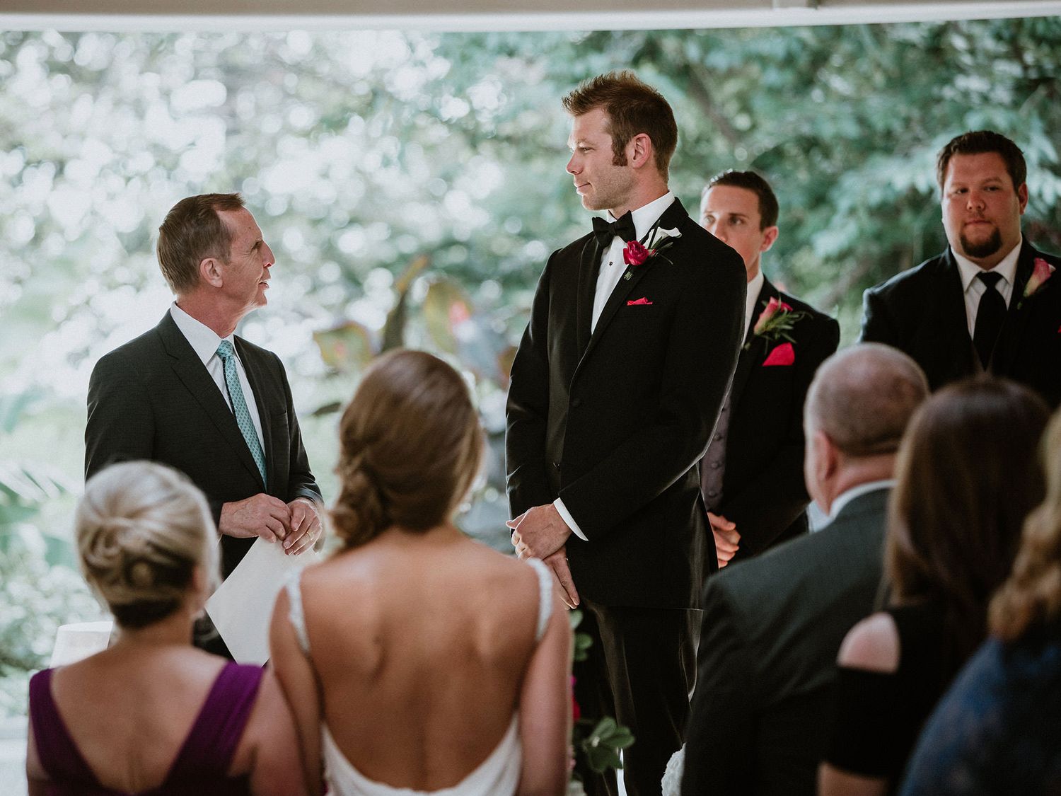 A group of wedding guests gather outdoors under trees during an emotional ceremony moment.