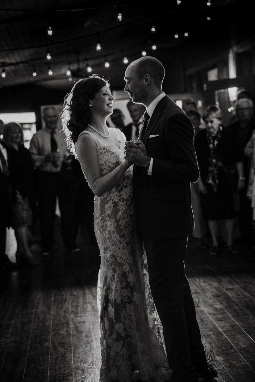 A couple shares their first dance at a wedding reception in a dimly lit venue with romantic lighting and guests watching.