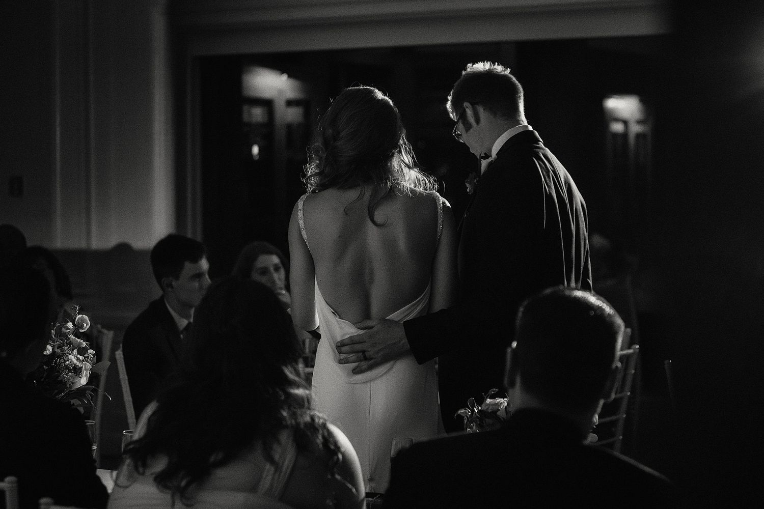 A black and white photo of a bride and groom giving their speech in low-light settings creating a moody, cinematic atmosphere.