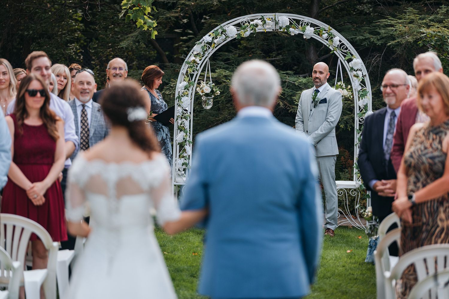A groom watches as his bride and her father make their way up the aisle during a wedding ceremony.
