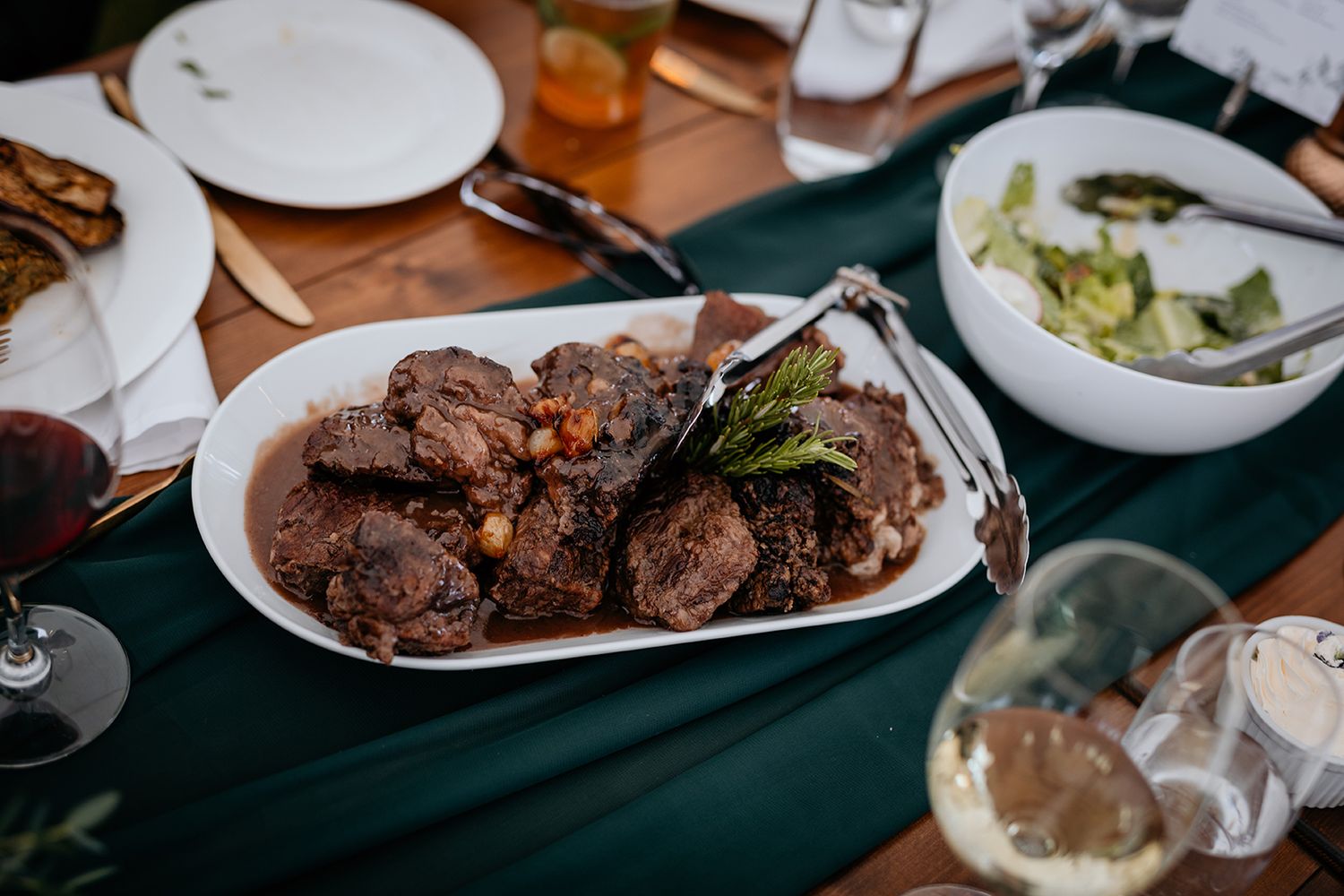 A platter of grilled meat served on a white plate with green garnish on a dark tablecloth.