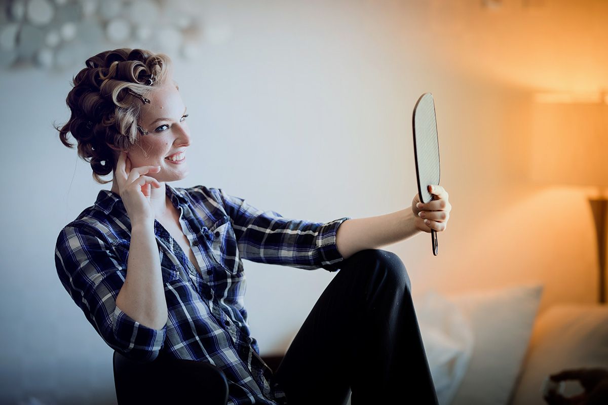 A woman in a plaid shirt checks out her hair in a hand-held mirror.