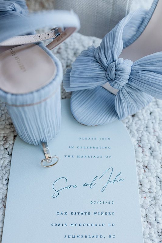 Light blue wedding invitation details with elegant bow design and delicate lace background in soft pastel tones.
