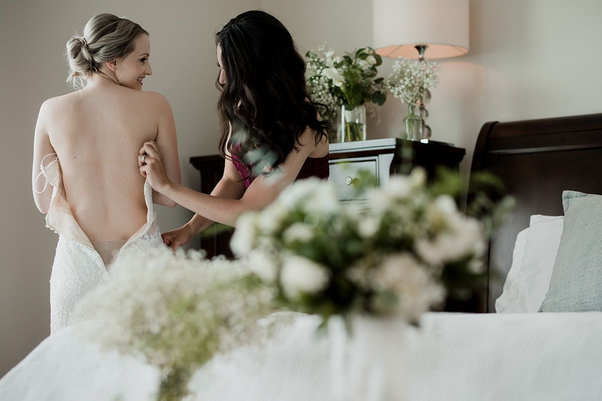 A bride-to-be shows her bare back as a woman helps her put on her wedding gown.