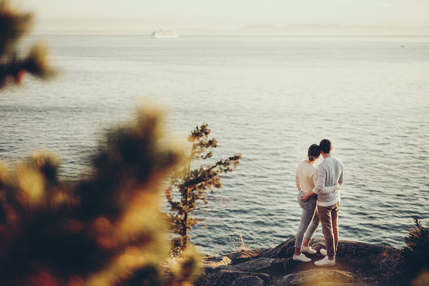 A couple sits together on a wooden dock overlooking a serene lake during sunset.